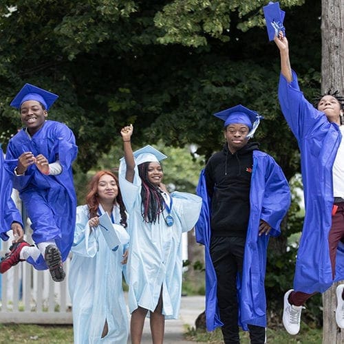 In Photo: CAP students in cap and gown jumping for joy