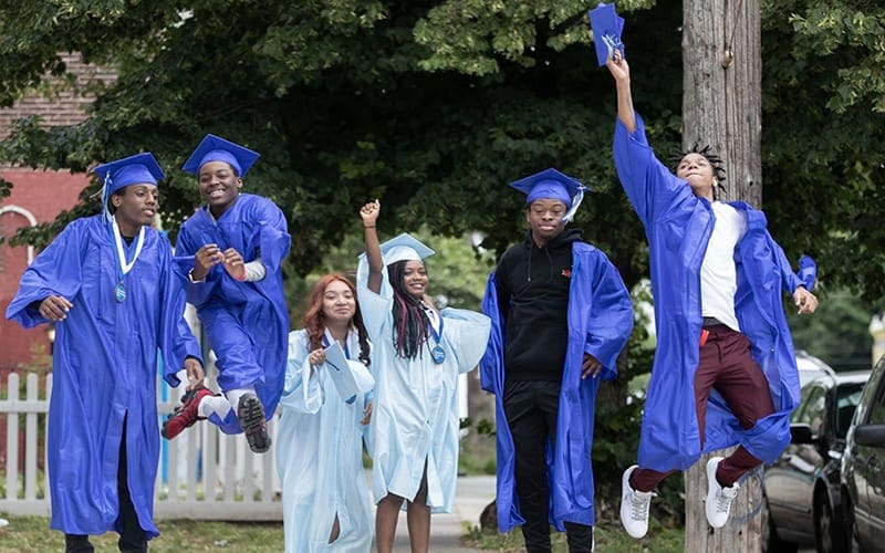 In Photo: CAP students in cap and gown jumping for joy