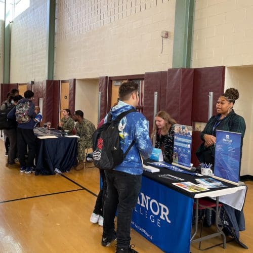 Student and college representative talking over a display table in a high school gym.