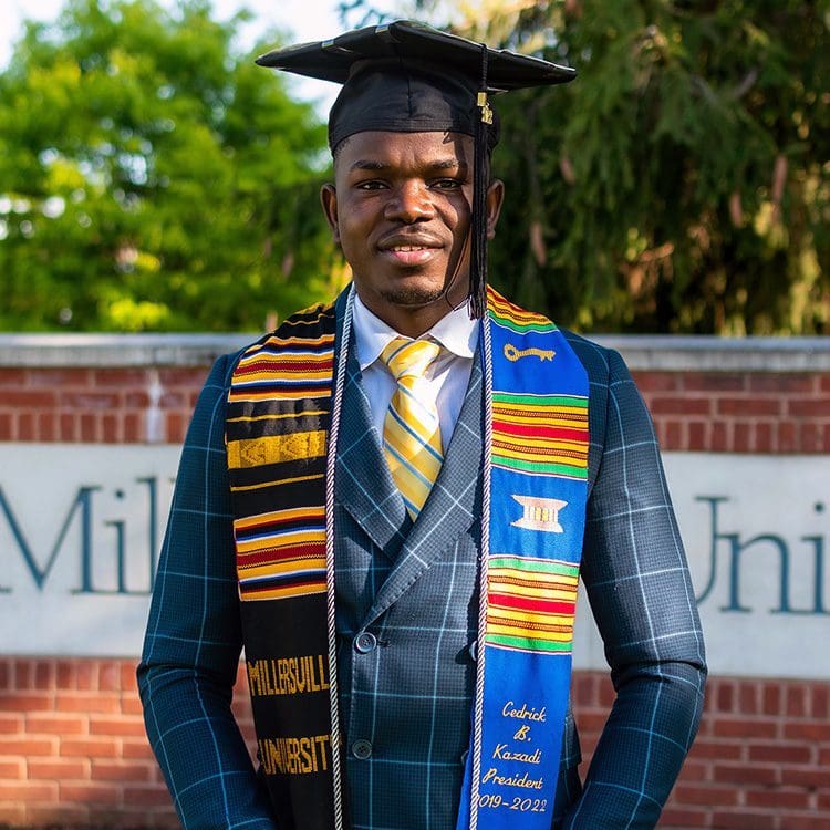 Young Black man in suit with mortarboard cap outside at Millersville University.